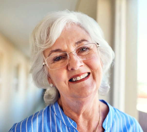 Smiling older woman with white hair and glasses wearing blue striped shirt indoors