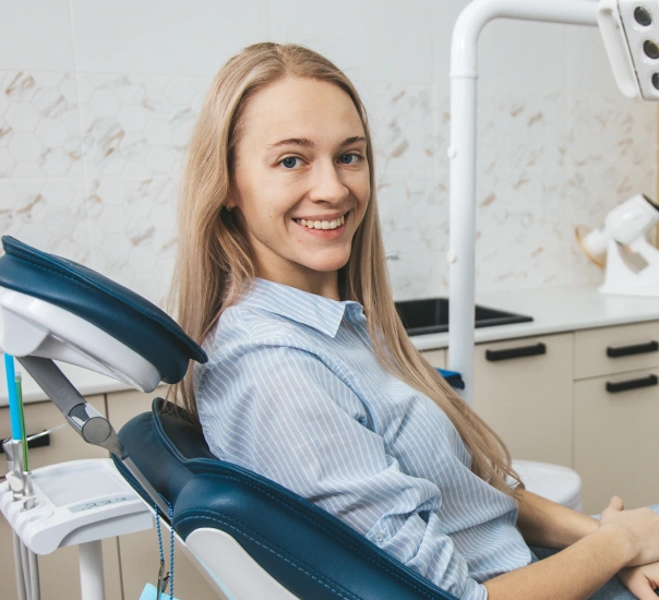 Female dentist in light blue shirt smiling in modern dental office operatory