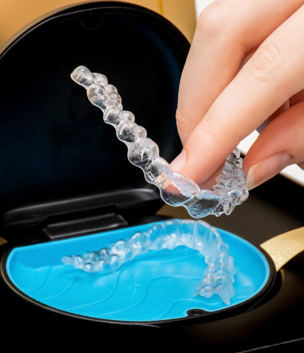Clear orthodontic aligner being removed from blue dental tray during treatment demonstration.