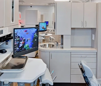 Modern dental office operatory with treatment chair, digital displays, and white cabinetry.