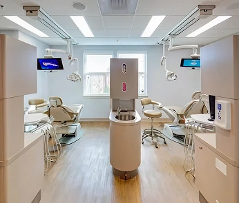 Modern dental operatory with two treatment chairs, overhead lighting, and sterile equipment setup.