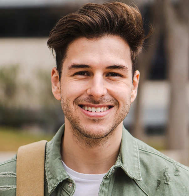 Young man smiling at camera wearing sage green jacket, outdoor professional headshot.