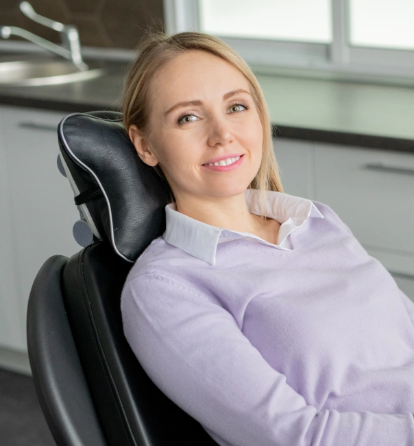 Professional woman in lavender shirt seated in dental chair, office setting background.
