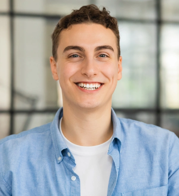 Young man smiling at camera wearing light blue shirt in modern office setting