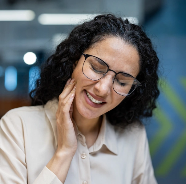 Woman wearing glasses and white coat smiling in modern dental office setting.