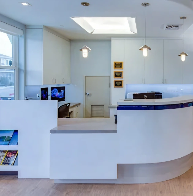 Modern dental office reception area with curved white desk and contemporary lighting fixtures.